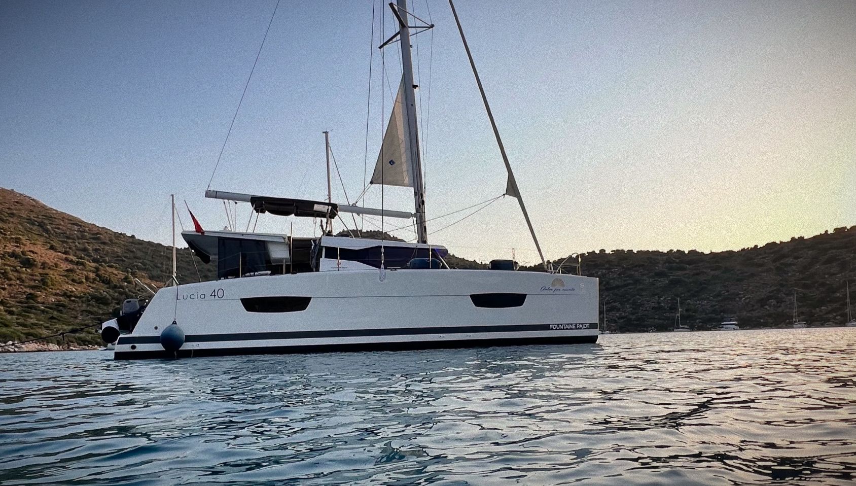 Катамаран Fountaine Pajot 40 «Dolce» на якоре в бухте на закате, рядом холмы