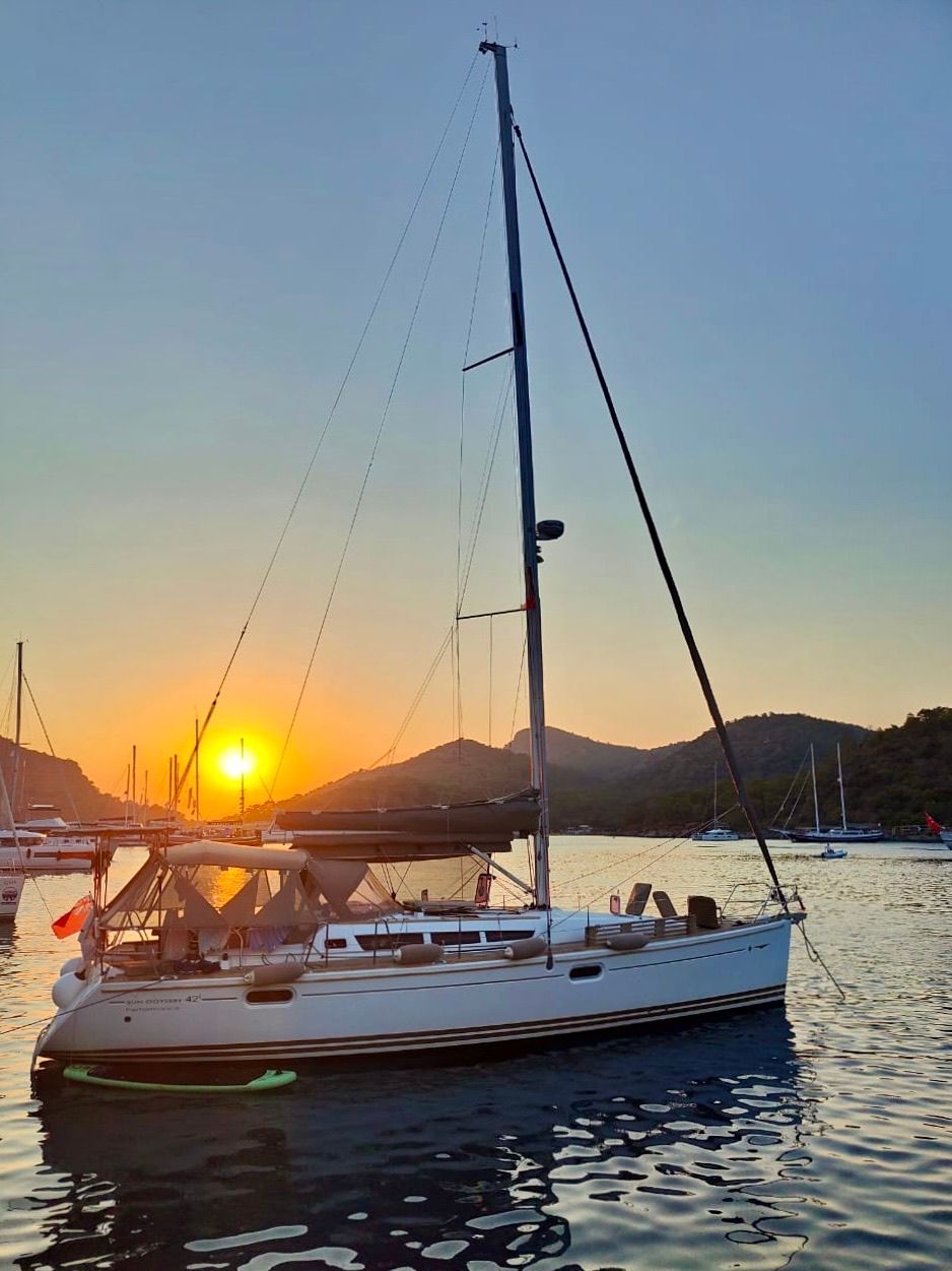 Яхта Sun Odyssey 42 на закате в бухте у гор, на корме турецкий флаг